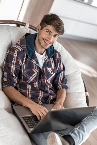 Lachende kerel met een laptop zittend in een stoel — Stockfoto