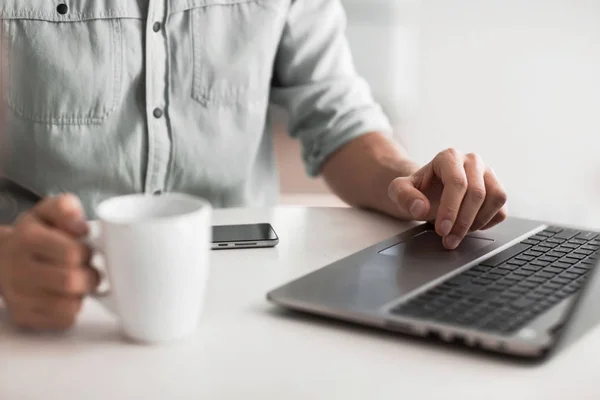 Närbild. en man som arbetar på en bärbar dator sitter vid ett bord — Stockfoto