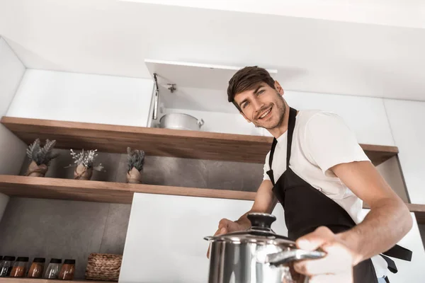 Улыбающийся мужчина с горшком, стоящим на домашней кухне — стоковое фото
