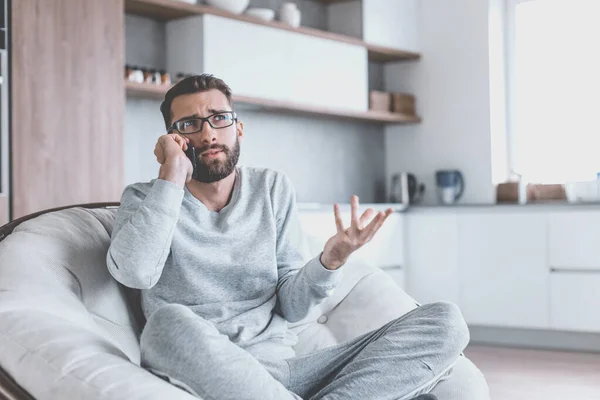 Hombre alegre hablando en un teléfono móvil sentado en una silla cómoda — Foto de Stock