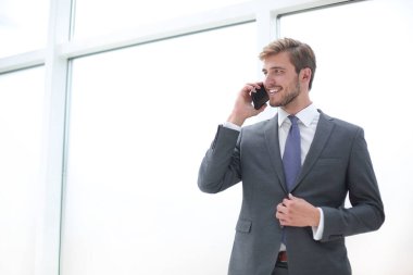 ofis penceresinin yanında duran bir cep telefonu yla konuşan işadamı