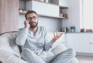 Rahat bir koltukta oturan neşeli bir adam cep telefonuyla konuşuyor.