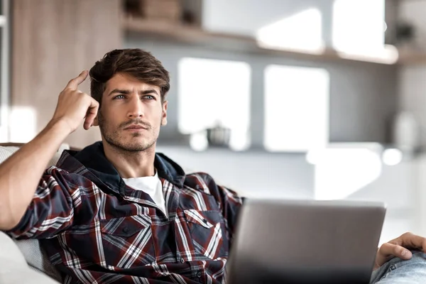 Närbild. drömmer ung man sitter framför en öppen laptop — Stockfoto