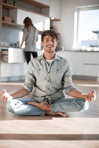 Jovem sentado na posição Lotus no chão da cozinha — Fotografia de Stock