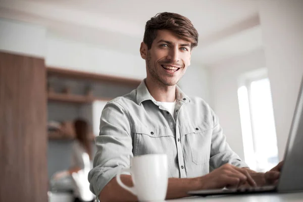 Jonge man zitten in de voorkant van open laptop in keuken — Stockfoto