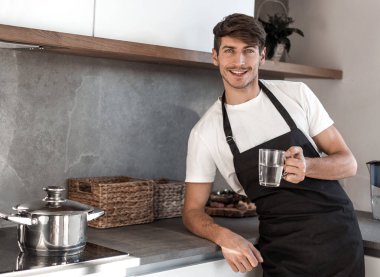 Mutfakta elinde bir bardak suyla gülümseyen genç adam..