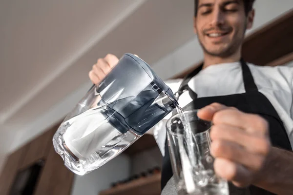 Молодой человек наливает чистую воду в стакан — стоковое фото