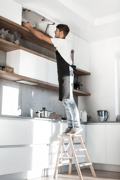 Hombre de pie sobre una escalera en la cocina del hogar — Foto de Stock