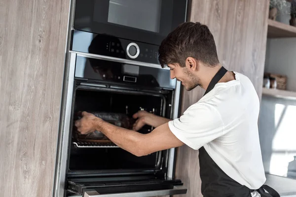Homem abrindo o forno na cozinha da casa — Fotografia de Stock