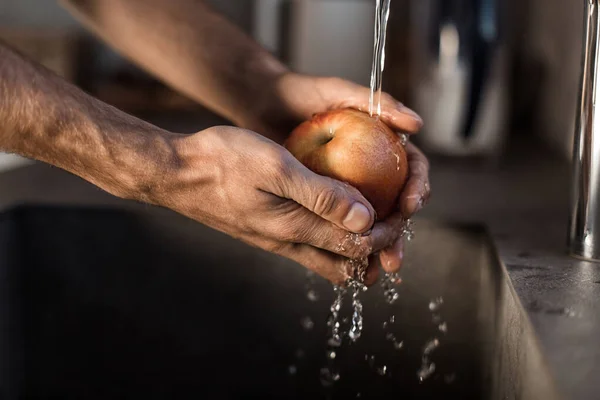 Close-up. een man wast een appel onder de kraan — Stockfoto