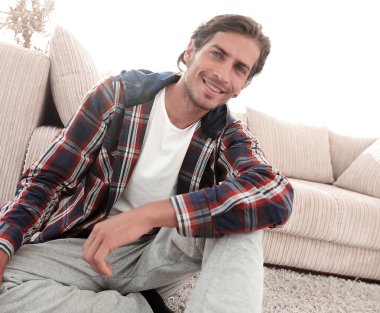 Kendine güvenen adam rahat bir oturma odasında halı üzerinde oturan.