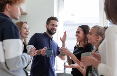 Bir grup mutlu erkek ve kadın çay içerken sohbet ediyorlar.