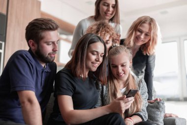 Neşeli genç adam oturmuş ve şaşırmış bir şekilde akıllı telefon kullanıyor.