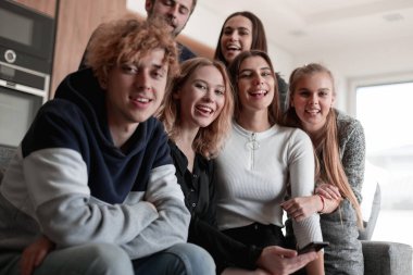 Neşeli genç adam oturmuş ve şaşırmış bir şekilde akıllı telefon kullanıyor.