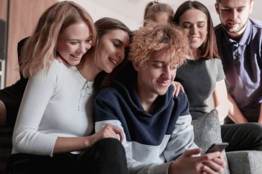 Neşeli genç adam oturmuş ve şaşırmış bir şekilde akıllı telefon kullanıyor.