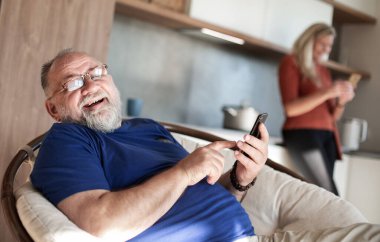 Evde oturan akıllı telefonlu yaşlı bir adam..