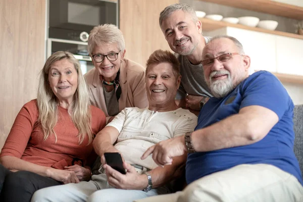 Grupo de amigos mais velhos com um smartphone sentado em uma sala de estar aconchegante . — Fotografia de Stock