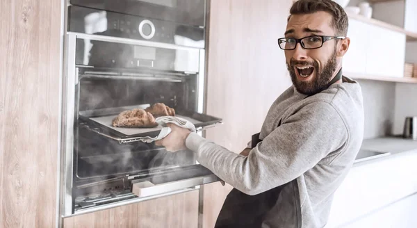 På nära håll. En ung man tar fram ugnsbrickan med croissanter. — Stockfoto