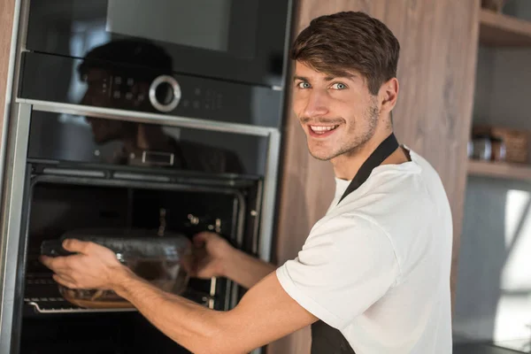 Smiling young man warming up dinner in his kitchen — Stock Photo, Image