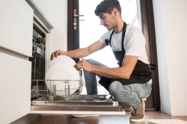 Gülümseyen genç adam bulaşık makinesinden temiz tabakları çıkardı.