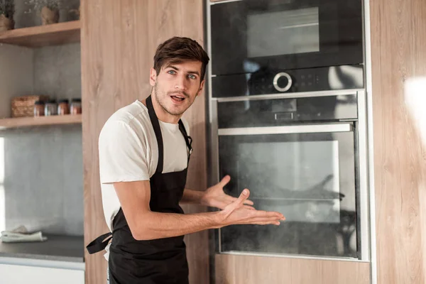 Emotional young man standing near broken oven — Stock Photo, Image