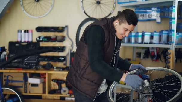 Knappe monteur is het reinigen van fietswiel buiten en binnen, naaf en spaken met stuk doek en luisteren naar muziek met koptelefoon. Beroep en mensen concept. — Stockvideo