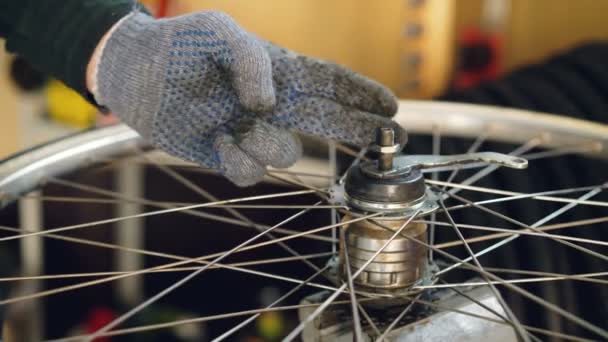 Primer plano plano de la mano masculina en el mecanismo de montaje de guantes de protección de la rueda de bicicleta que aprieta el tornillo de metal. Trabajo, personas y concepto de profesión . — Vídeo de stock