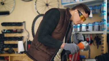 Genç yakışıklı adam profesyonel tamirci elektrik daire testere ile çalışma, küçük metal yedek parça testere ile kesme ve onun işyerinde müzik.