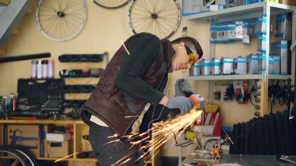 维修人员在工作的小工作场所使用电动圆锯。年轻人戴着防护眼镜和手套, 正在用耳机听音乐。. — 图库视频影像