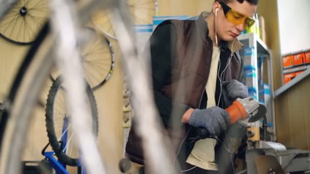 Ein junger, gut aussehender, erfahrener Servicetechniker setzt in seiner Werkstatt eine elektrische Kreissäge ein. Mann in Schutzbrille und Handschuhen schaut auf Säge und hört Musik. — Stockvideo