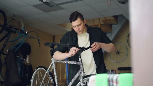 Skilled mechanic is fixing handle-bar of modern bicycle using professional tools in workshop with spare parts and equipment. Bike maintenance and people concept. — Stock Video