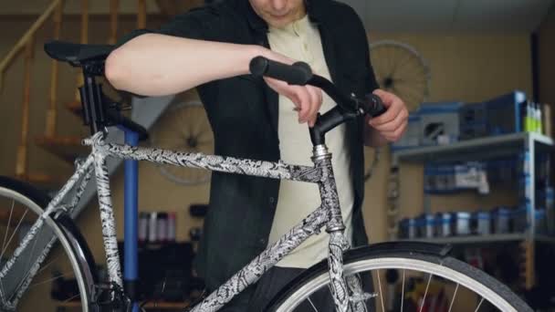 Tilt-up shot of young man bike repairman fixing broken handlebar of modern bicyle with tools. Ciclos de reparación, personas cualificadas, concepto de taller ocupado . — Vídeos de Stock