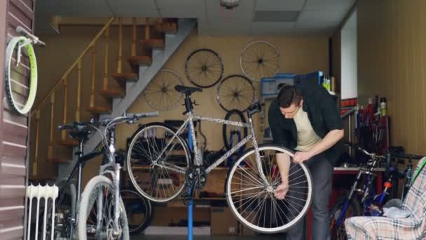 Mecánico masculino calificado es la fijación de la rueda de bicicleta con llave y luego girarlo y comprobar. Muchos ciclos, piezas de repuesto, herramientas y equipos son visibles . — Vídeos de Stock