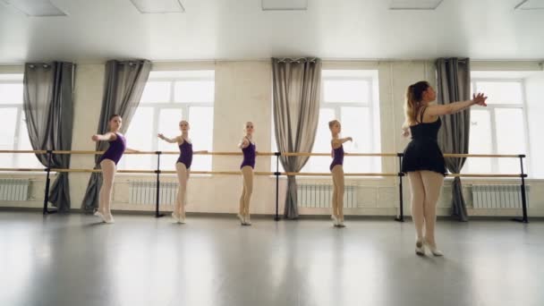 Επαγγελματική μπαλέτο Δάσκαλος διδάσκει κοριτσάκια για να ενεργοποιήσετε τις ισορροπήσεις και stretcg πόδια και τα χέρια ενώ νέοι χορευτές επανάληψη μετά δάσκαλος κρατώντας μπαλέτο μπαρ. — Αρχείο Βίντεο