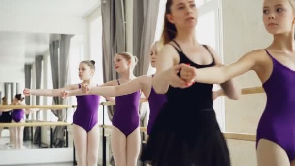 Начинающие артисты балета практикуют движения рук во время балетного класса в студии. Преподаватель профессиональной балерины учит их корректировать позиции и давать инструкции — стоковое видео