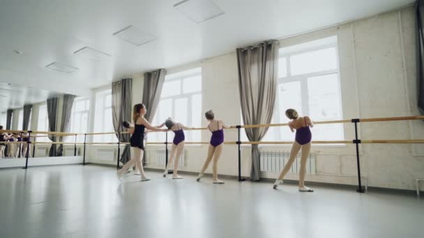苗条的女孩正在学习向后弯曲练习芭蕾运动在宽敞的灯光工作室与大窗户和芭蕾酒吧。有帮助的导师教他们. — 图库视频影像