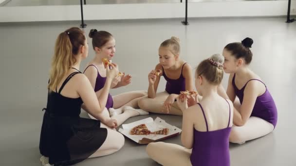 Los niños felices estudiantes de ballet y su maestro están comiendo pizza durante la pausa para el almuerzo entre clases de baile. Las niñas están hablando, sonriendo y disfrutando de la deliciosa comida . — Vídeo de stock