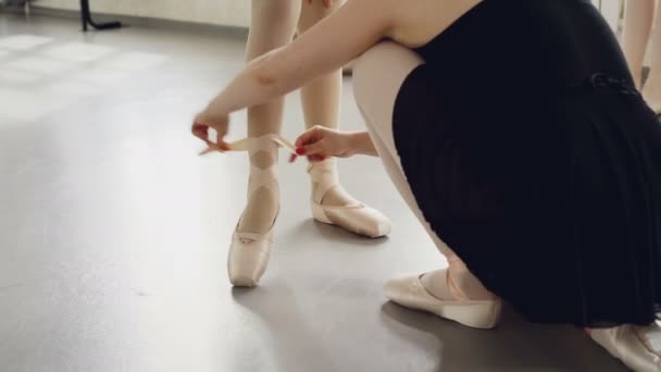 役に立つ先生は、バレエ レッスンの前に小さな足周りのリボンを結ぶ小さな生足でポワント シューズを入れています。振り付け、履物、人々 の概念. — ストック動画