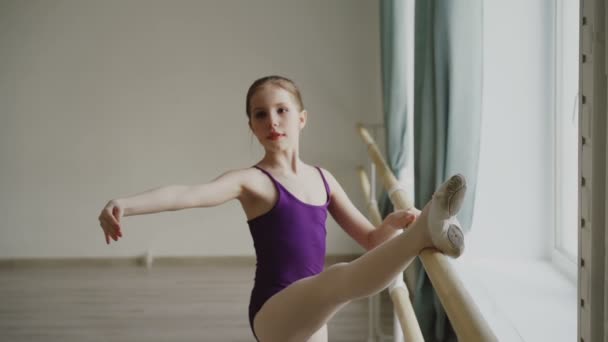 Slow motion of young slim ballerina practising alone at ballet barre in light ballroom during class in art studio. Pretty girl is wearing bodysuit and pointe-shoes. — Stock Video
