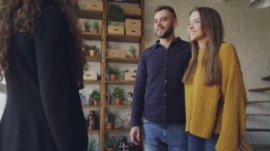 Mutlu genç çift yeni ev sonra sarılma ve gülüyor kadın emlakçı ile tokalaşırken alıyor. Yer değiştirme, mutluluk ve konaklama konsepti.