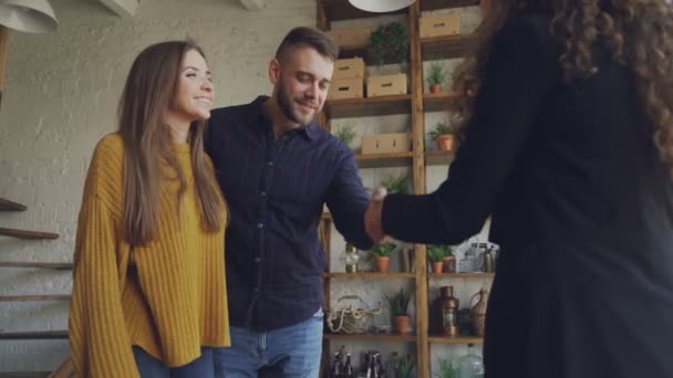 La pareja casada está comprando apartamento, estrechando la mano con la agente inmobiliaria femenina y luego abrazando, besando y riendo. Concepto de reubicación, felicidad y alojamiento . — Vídeos de Stock