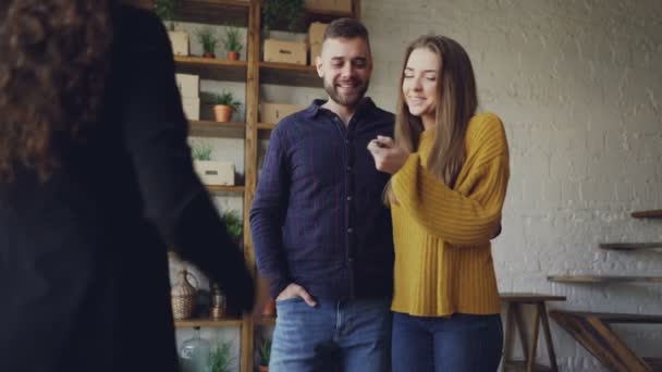 Agente de habitação está dando chaves para os compradores de novo apartamento, marido feliz e esposa estão abraçando e beijando, o homem está apertando as mãos com corretor de imóveis feminino . — Vídeo de Stock