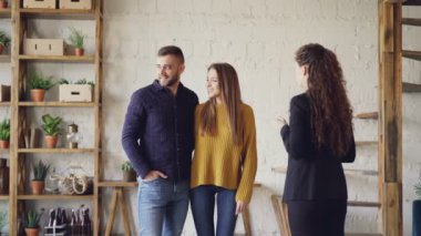 Takım elbiseli kadın emlakçı loft tarzı düz genç adam ve kadın daire arıyor için gösteriyor. Alıcılar iç hakkında heyecanlıyız, onlar gülümseyen ve söz.