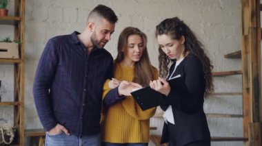 Genç istemcilerin belgeleri seyir ve yeni daire içinde dururken Emlak komisyoncusu ile anlaşma koşulları tartışıyor. Yer değiştirme ve satınalma kavramı.