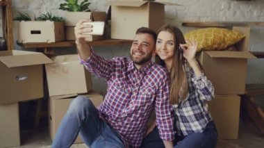Mutlu çift selfie yeni daire satın aldıktan sonra evin anahtarları ile alıyor. Gençler poz ve arka planda kutuları ile smartphone kameraya bakarak öpüşme.