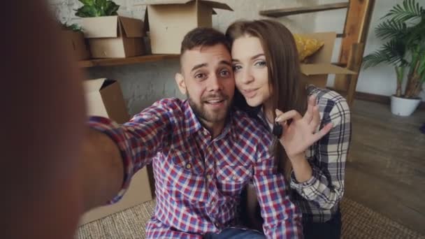 Punto de vista de la imagen de los jóvenes feliz pareja grabación de vídeo acerca de mudarse a una nueva casa juntos, hablando y mostrando las llaves. Concepto de juventud y recarga . — Vídeo de stock