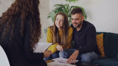 Seven erkek ve kız evi satın alacak plan seyir ve masada rahat kanepede oturan Emlak komisyoncusu konuşuyor.