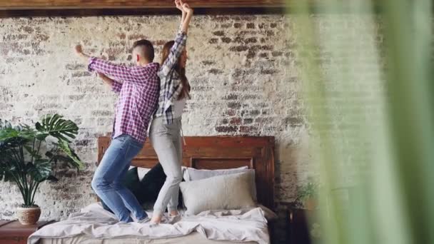 Movimento lento de jovens bonito e amoroso casal dançando se divertindo e rindo na cama em casa. Descuido, tempo livre e conceito de relacionamento . — Vídeo de Stock