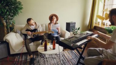 Amatör Grup şarkı ve iskambil gitar ve klavye mikrofon ve müzikal donanımları kullanarak ev stüdyosunda prova yapıyor. Bira şişeleri ve aperatifler görülebilir.