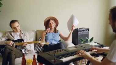 Neşeli genç insanlar müzik grubu şarkı ve klavye ve gitar çalmaya ev stüdyosunda pratik. Müzisyenler rahat kıyafetler giymiş.